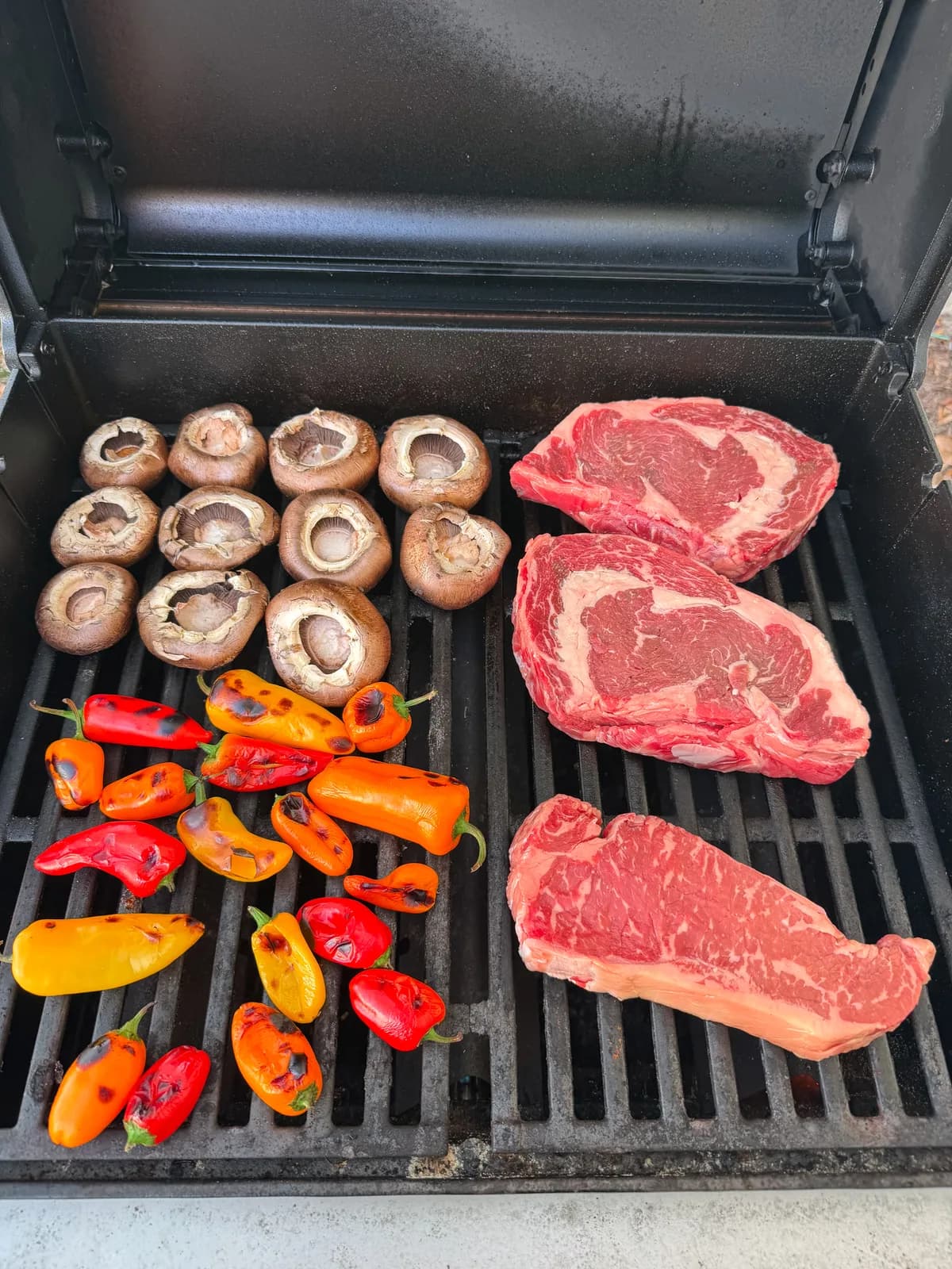 Steaks searing on an outdoor charcoal grill with smoke rising